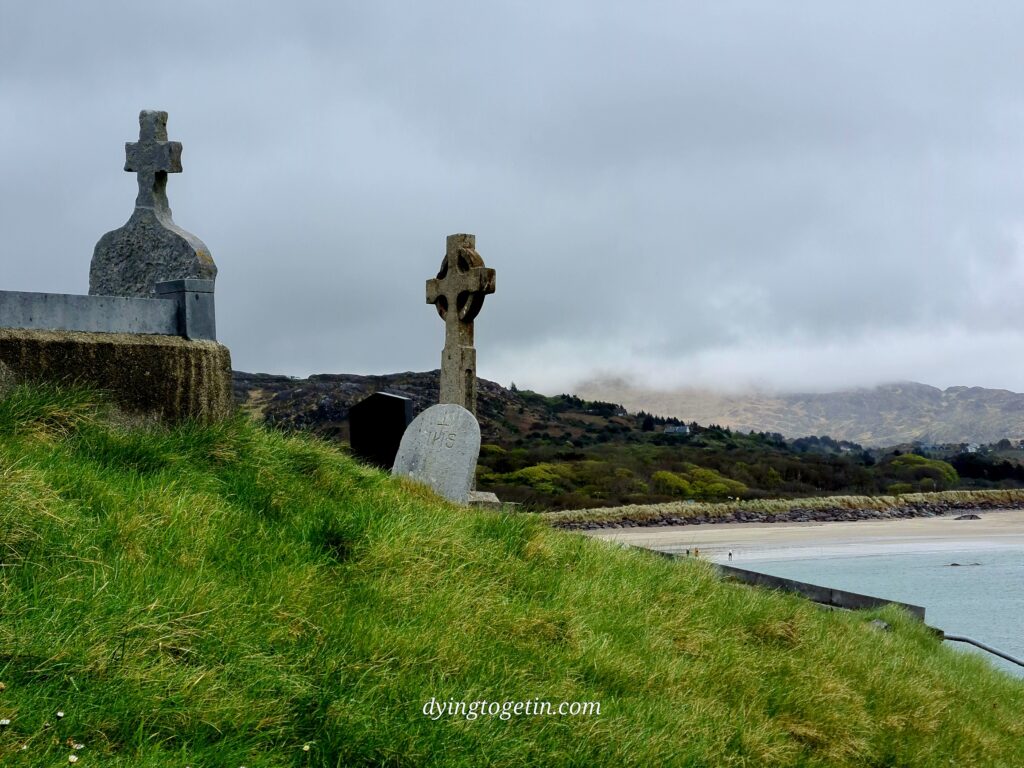 Headstones on a grassy knoll overlooking the sea and sand below