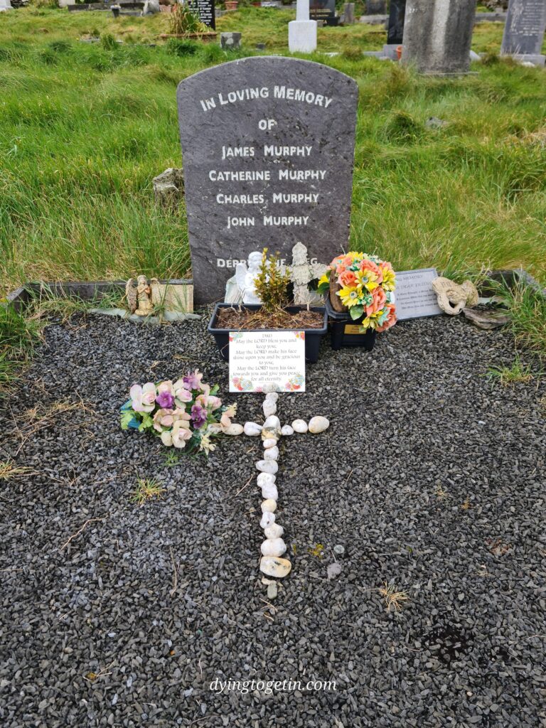 Tombstone that reads In loving memory of James Murphy Catherine Murphy Charles Murphy John Murphy Derr (rest of text blocked by ceramic angel and shell cross. Other ornaments and flowers scattered on the grave