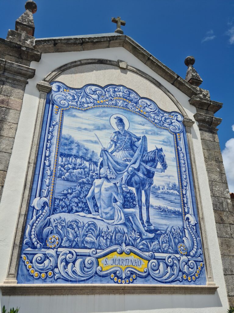 Blue and white tile fresco with yellow accents showing a roman soldier on a horse tearing his cloak in two to share with a near-naked beggar seated on the ground