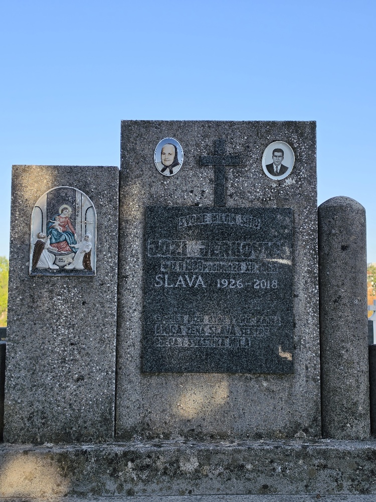 A large dark stone grave monument with two oval portrait photographs, a cross, religious imagery, and engraved memorial text.