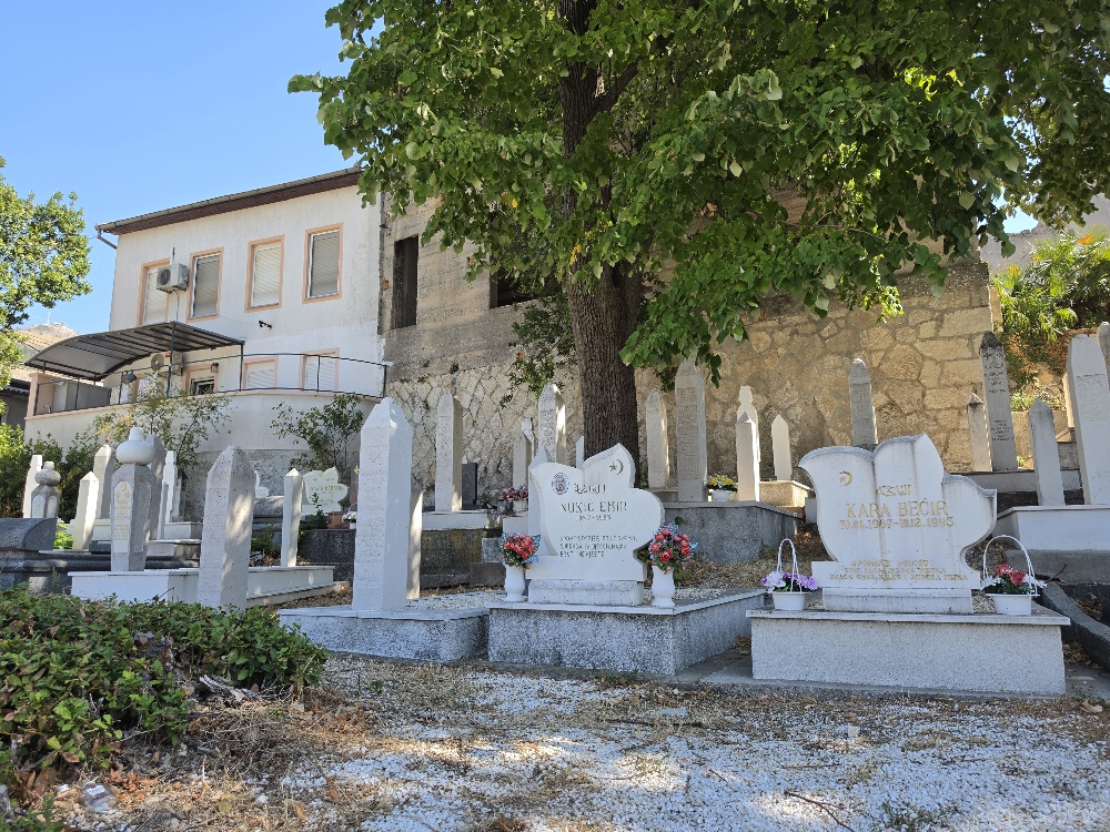 “White marble Muslim grave monument for Emir Nušić, marked ‘El Fatiha!’ and decorated with a portrait photograph, surrounded by traditional upright nišan gravestones.”