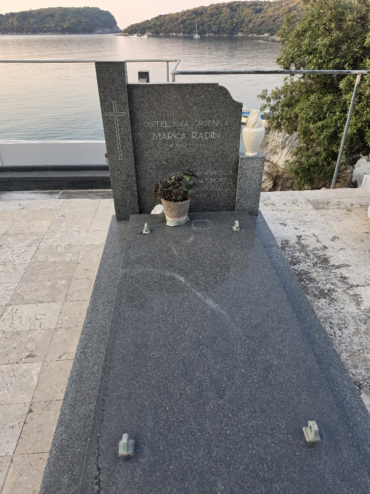 A polished dark-granite family tomb marked “Obiteljska grobnica Marko Radin,” overlooking the Adriatic Sea.